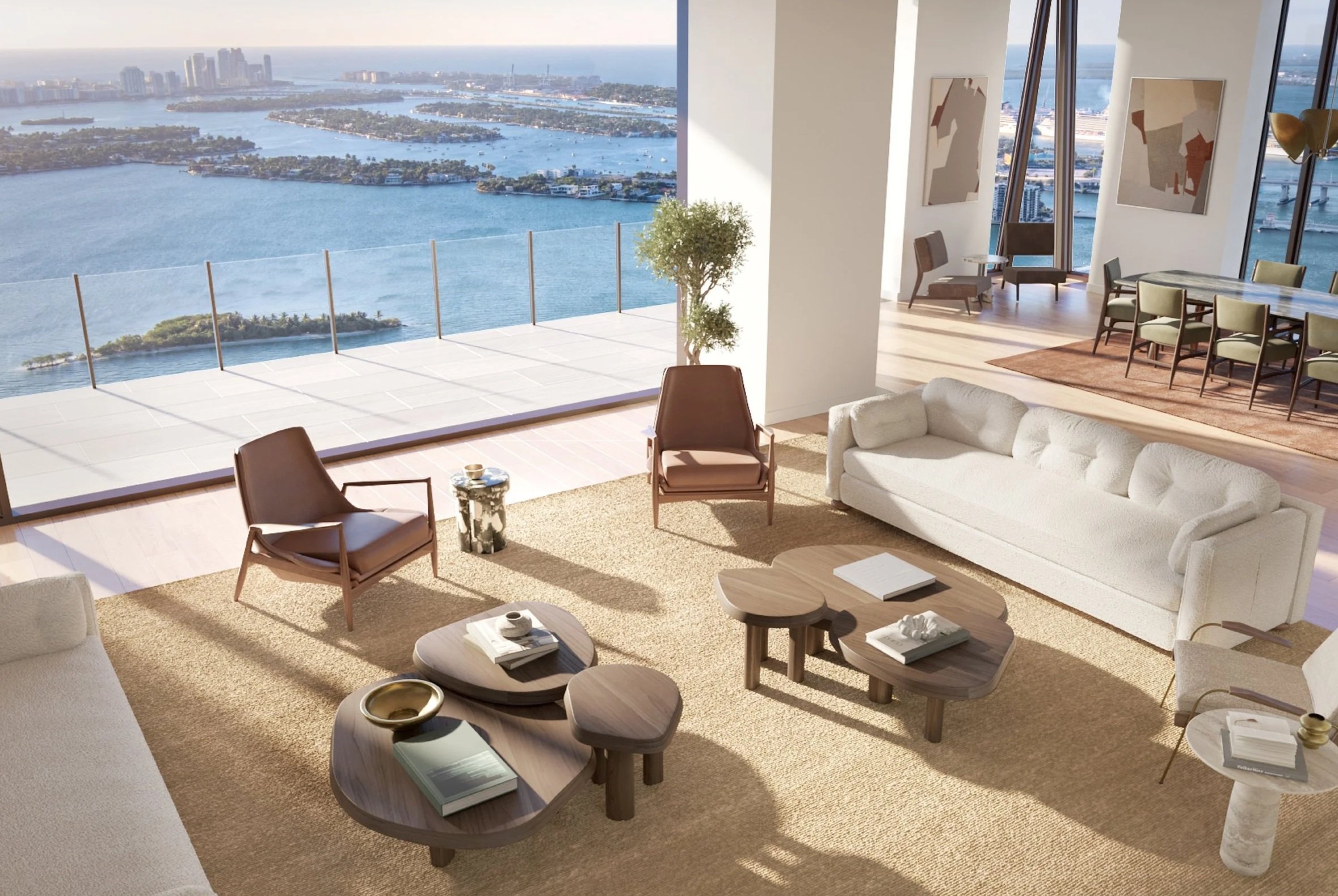 Modern living room with large windows overlooking a waterway cityscape, featuring a white sofa, two brown armchairs, and a wooden coffee table.