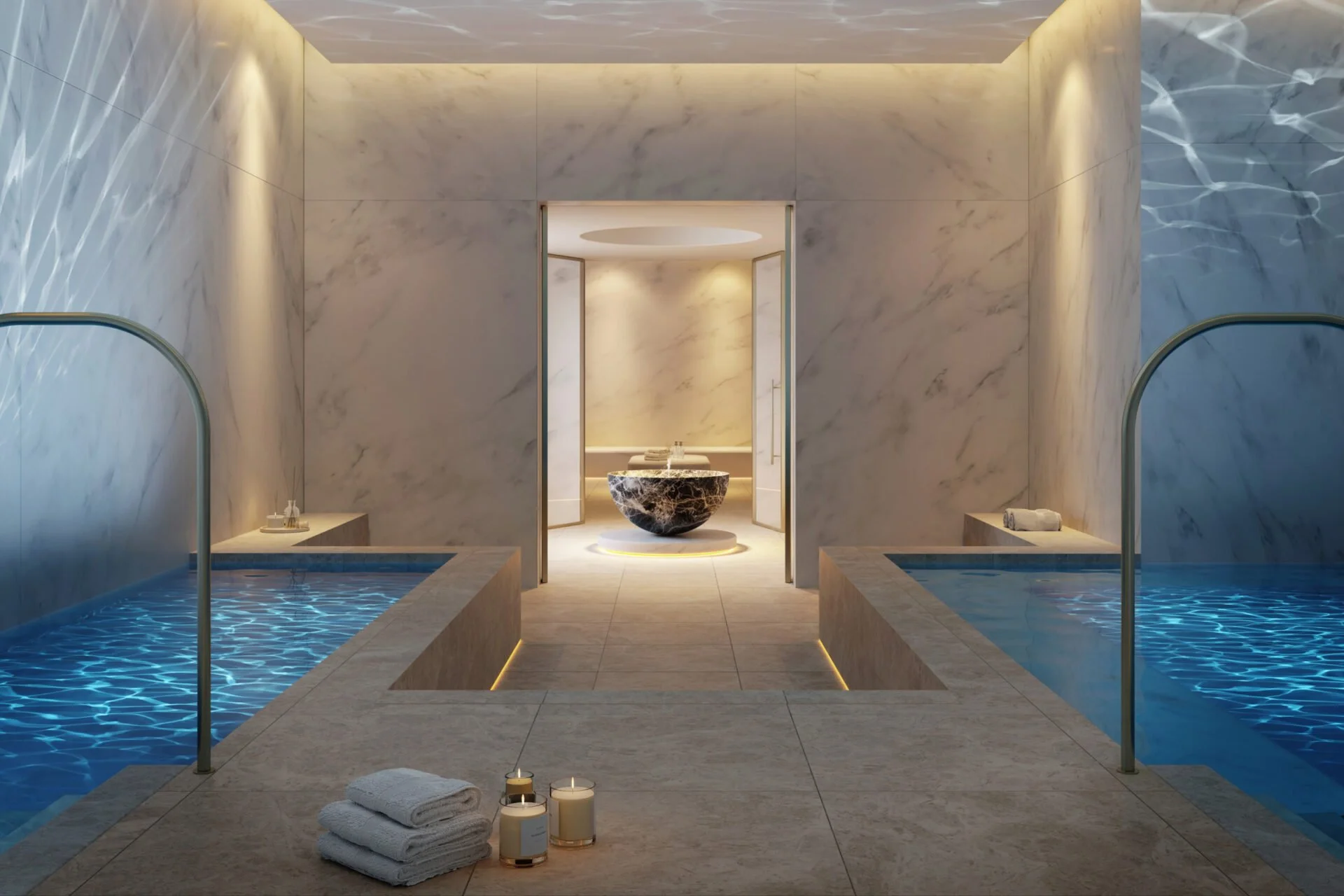 Luxurious spa room with two small pools on either side and a marble basin in the center of the back room, with folded towels and candles in the foreground.