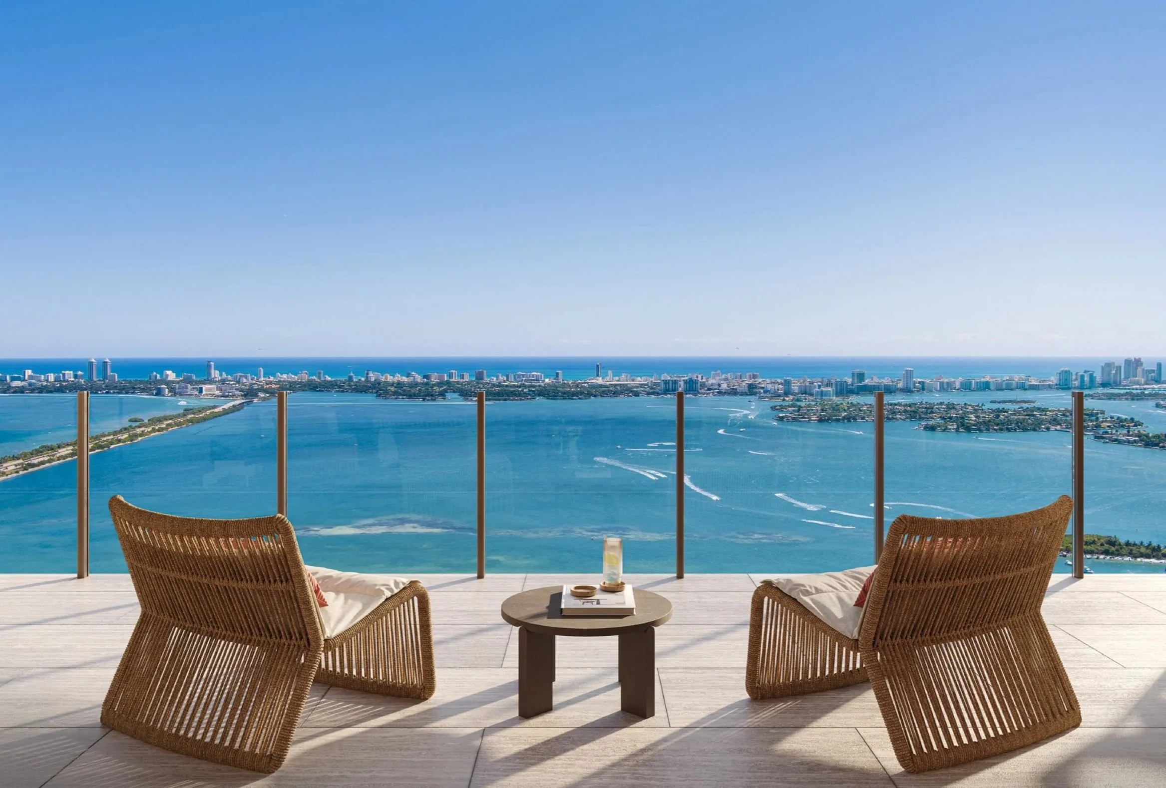 Balcony with two wicker chairs and a small round table overlooking a city skyline and water.