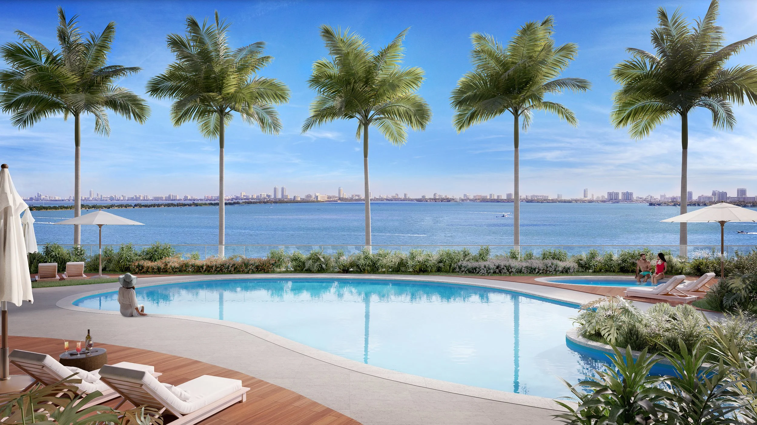 Luxury swimming pool area overlooking a large body of water and a city skyline in the distance. The pool is surrounded by white lounge chairs, umbrellas, green plants, and tall palm trees.