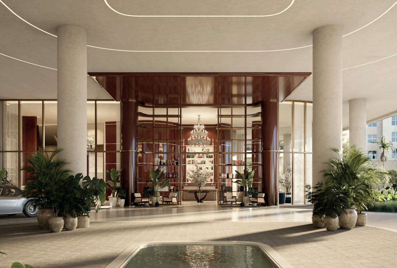 Lobby area with large, round concrete columns, a water feature in the foreground, and a reception desk with shelving and a chandelier in the background. Potted plants are placed around the space.