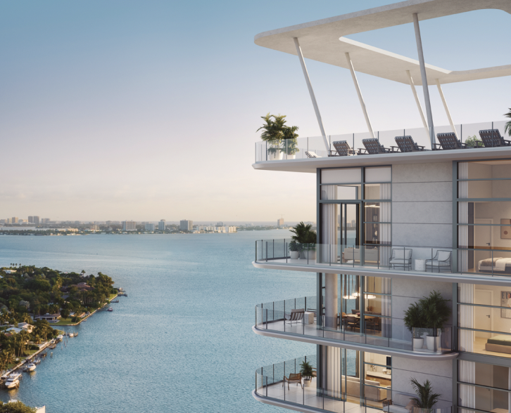 Modern high-rise apartment building with balconies overlooking water, with panoramic view of city skyline in the distance, during daytime.