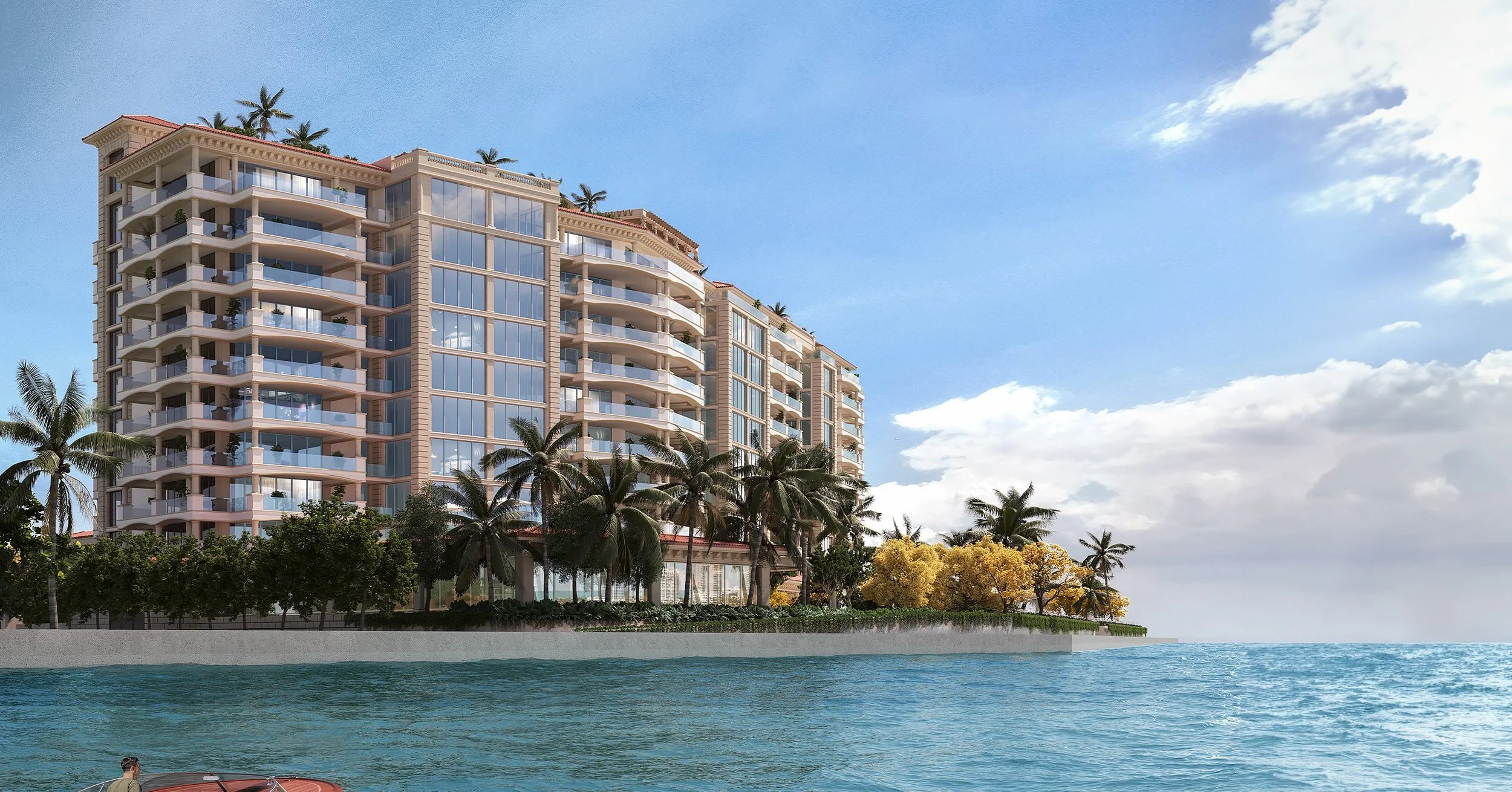 A high-rise residential building with balconies and glass windows situated by the water, surrounded by palm trees and other tropical vegetation, under a partly cloudy sky.