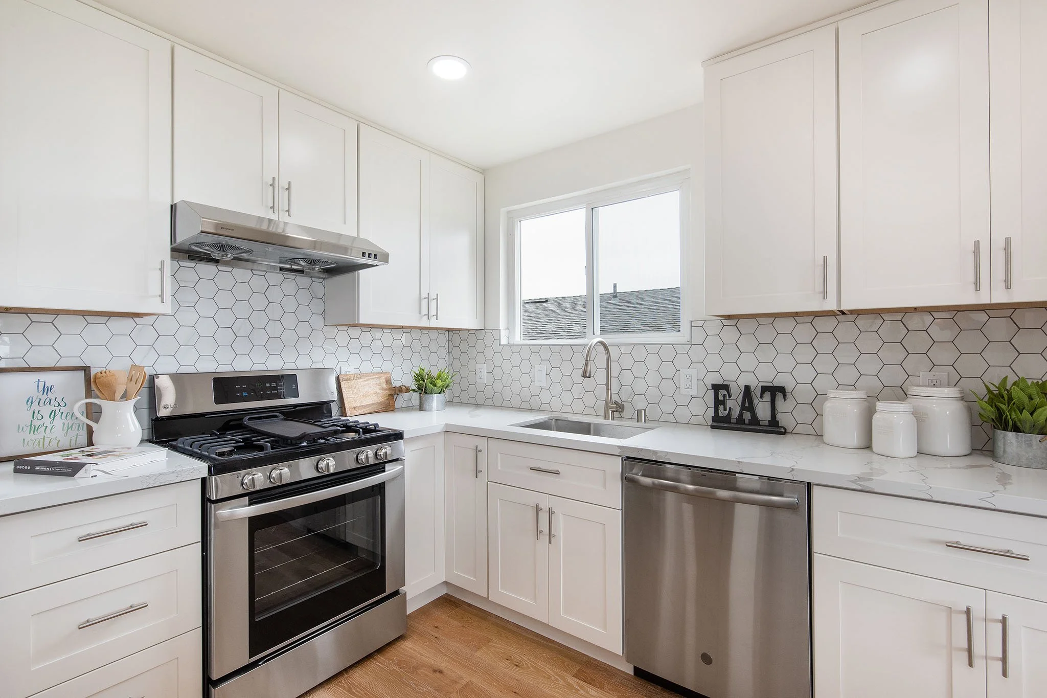 Modern white kitchen with stainless steel appliances, hexagon tile backsplash, and natural light from window.