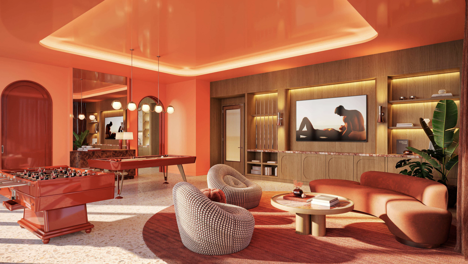 A vibrant living room with pink and orange hues, featuring modern furniture including a curved orange sofa, patterned armchairs, a round coffee table, a foosball table, and a ping pong table. The room has warm lighting, built-in shelves, a flat-screen TV, and green plants.