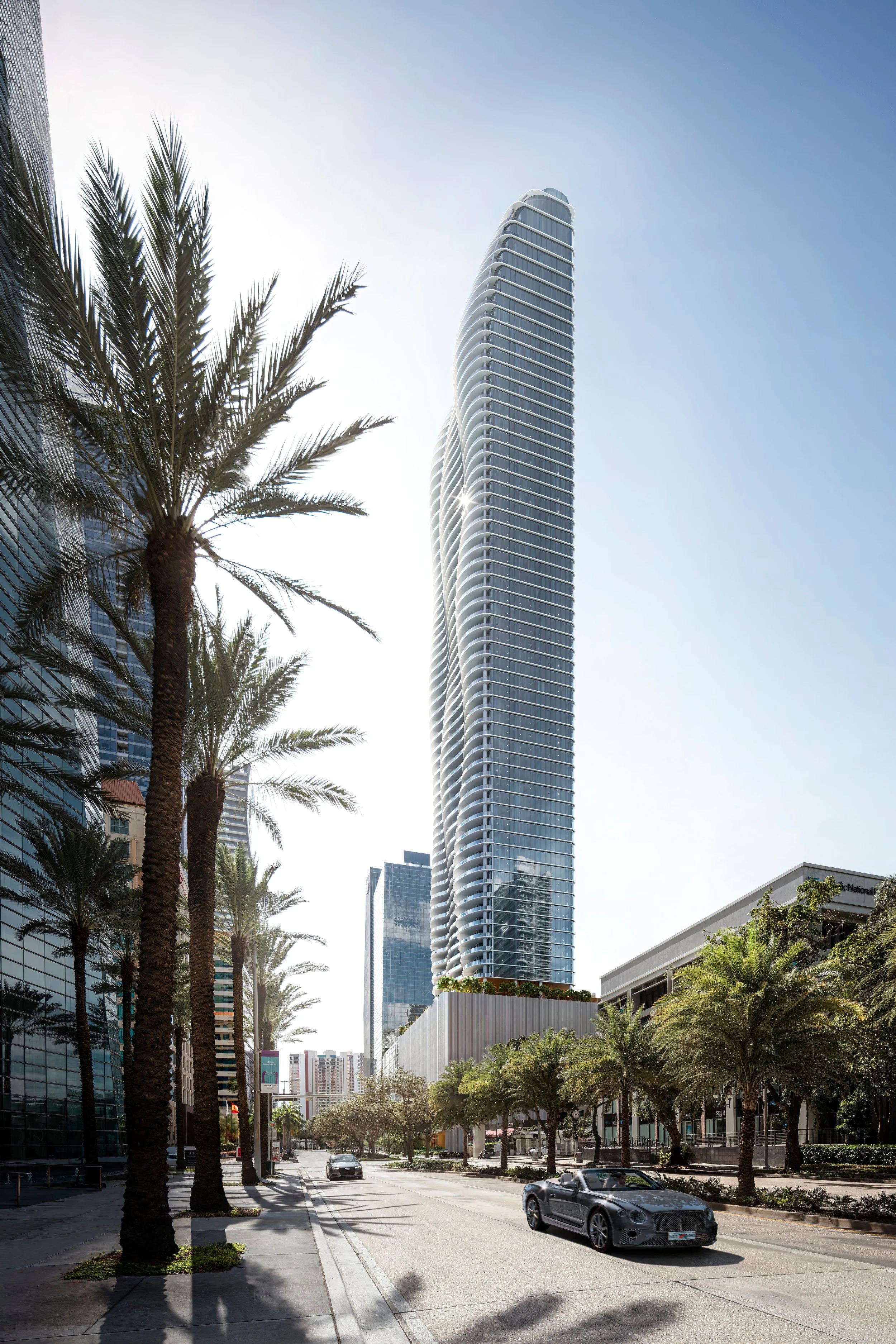 Tall modern skyscraper under a clear blue sky with palm trees lining the street below.