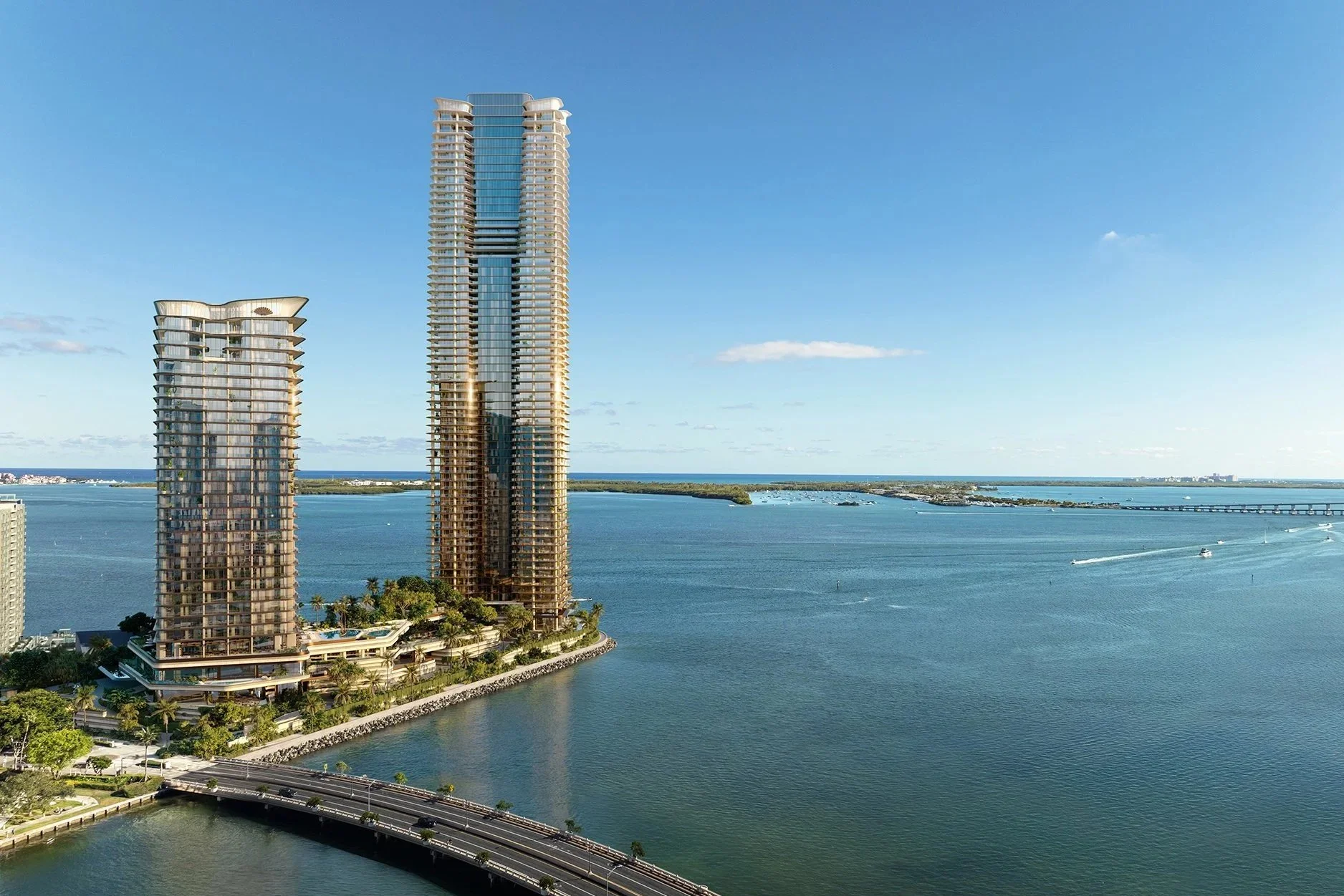 View of two tall modern high-rise buildings near a water body with a bridge in the background under a clear blue sky.