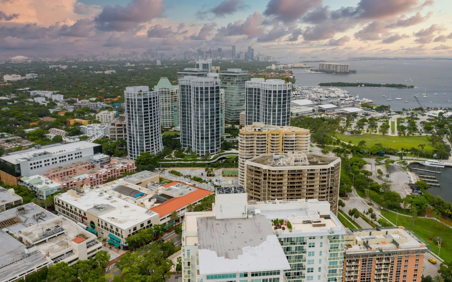 Aerial view of a city skyline with tall buildings near a water body, boats docked at a marina, and green parks in the foreground during daytime.