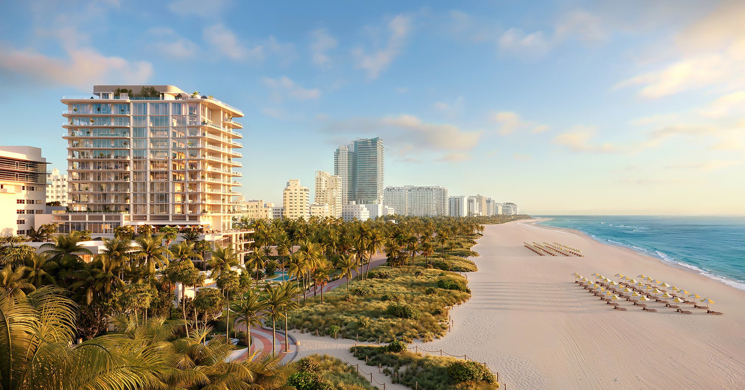 A view of a beach resort with high-rise buildings, palm trees, sandy shore, and beach chairs with umbrellas under a partly cloudy sky.