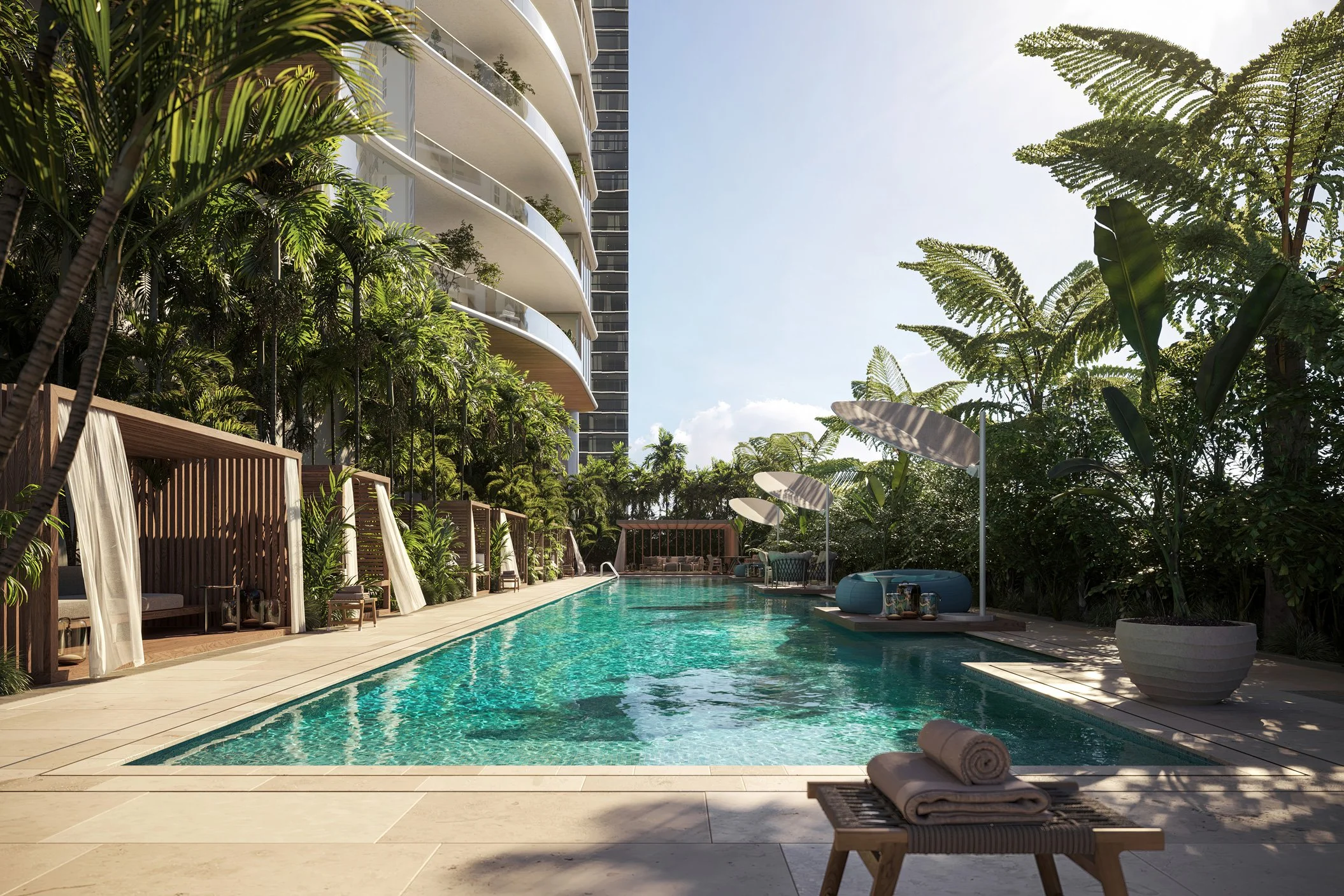 Luxury outdoor pool area surrounded by lush green plants and trees, with cabanas on the side and a modern building in the background, under a clear blue sky.
