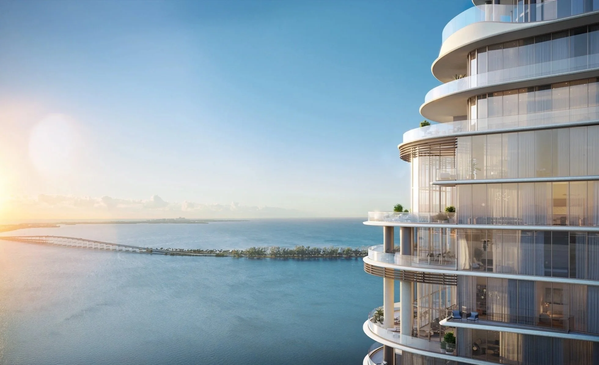 Modern high-rise building with glass balconies overlooking a body of water with a bridge in the distance, during sunset.