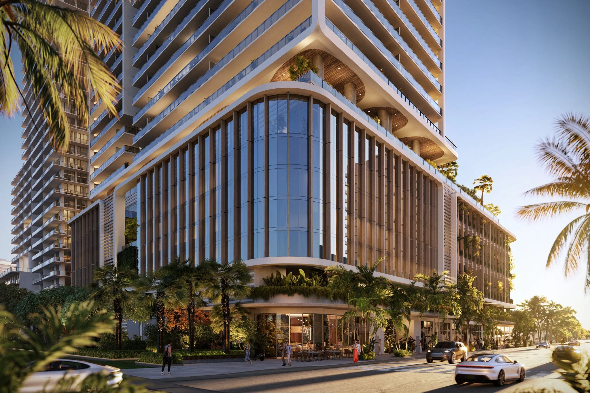 A modern multi-story building with glass and wooden elements, surrounded by palm trees and people walking on the sidewalk, and cars on the street, at sunset.