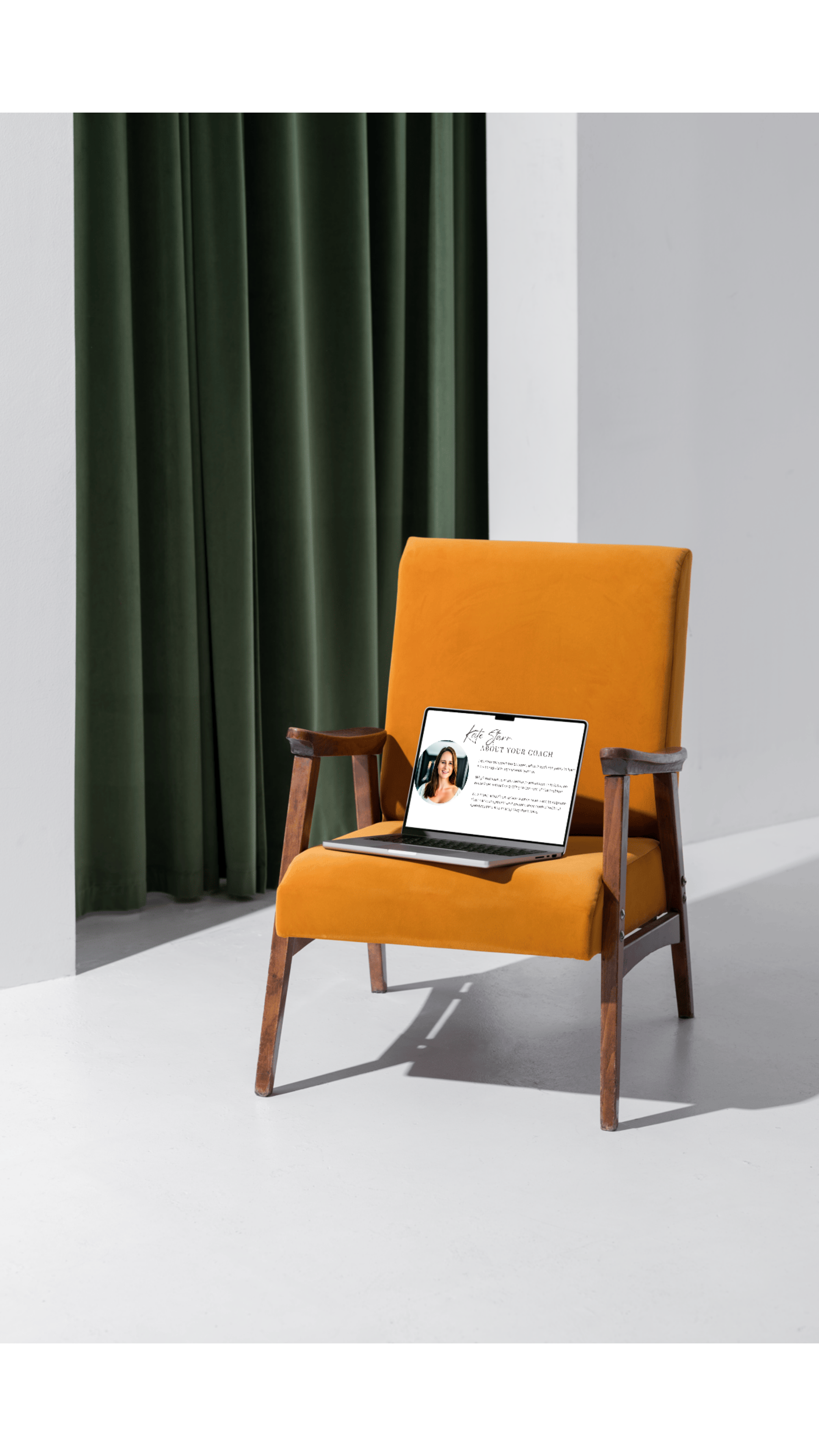 An orange armchair with wooden arms and legs, placed in front of a white wall and dark green curtains. A laptop displaying a coaching profile is on the chair's seat.