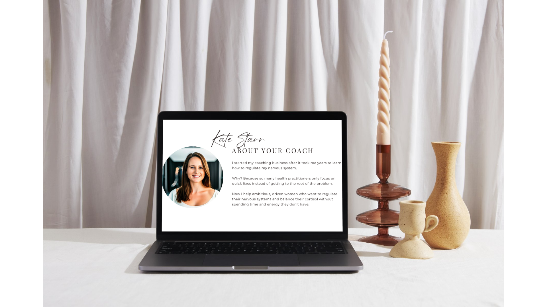 Laptop displaying a coaching profile page next to ceramic vases and a twisted candle on a white table with a white curtain background.