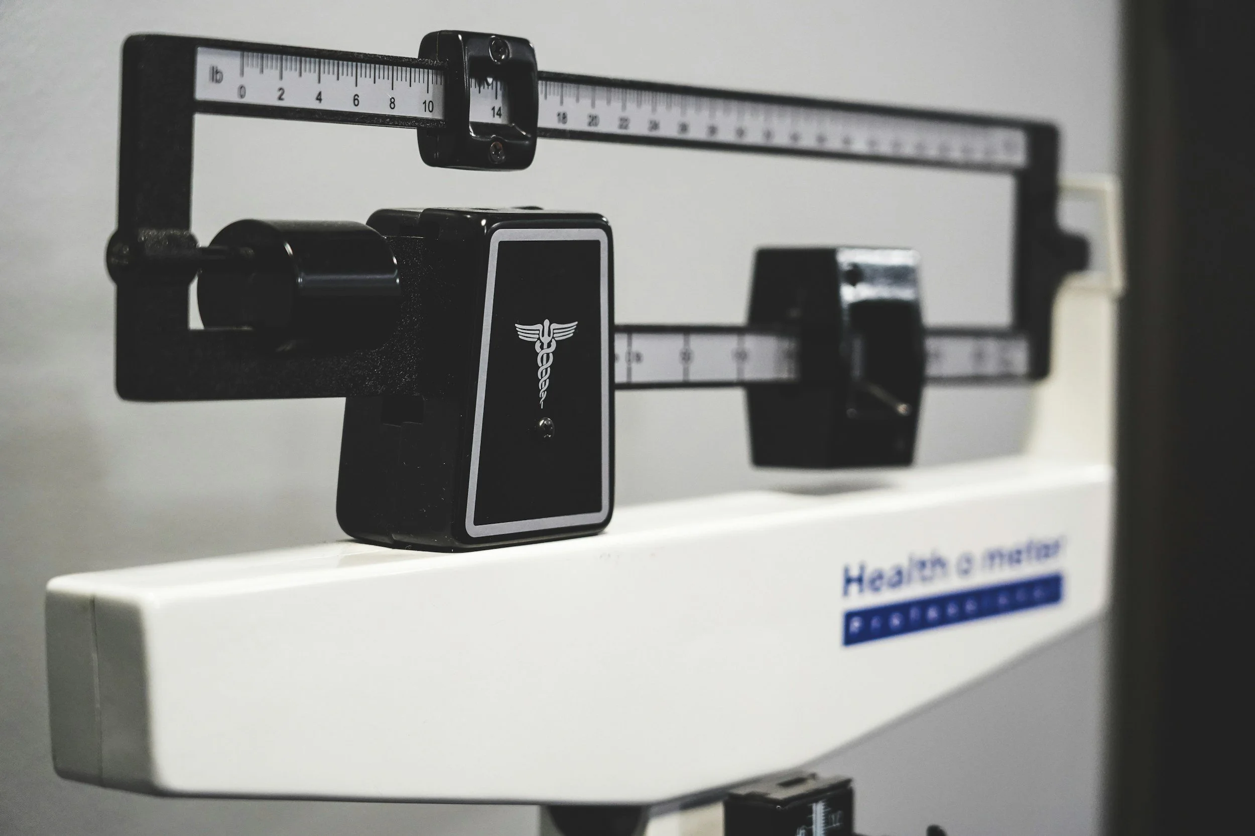 Close-up of a black and white medical weighing scale with a digital display and medical logo.