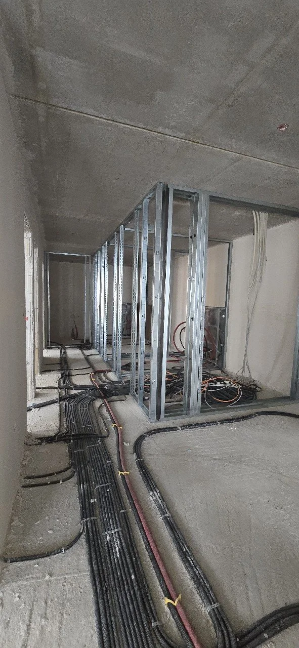 Baustelle mit Metallrahmen für Wandkonstruktion und installierten Elektrokabeln auf einem Rohfußboden
