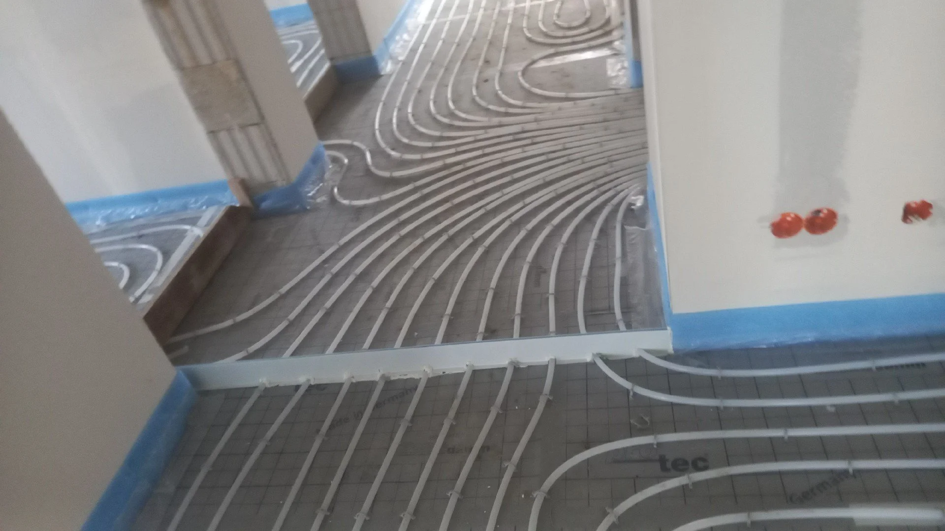 Fußbodenheizung Installation in einem Raum, mit sichtbaren Rohren, die für die Fußbodenverlegung vorbereitet werden.
