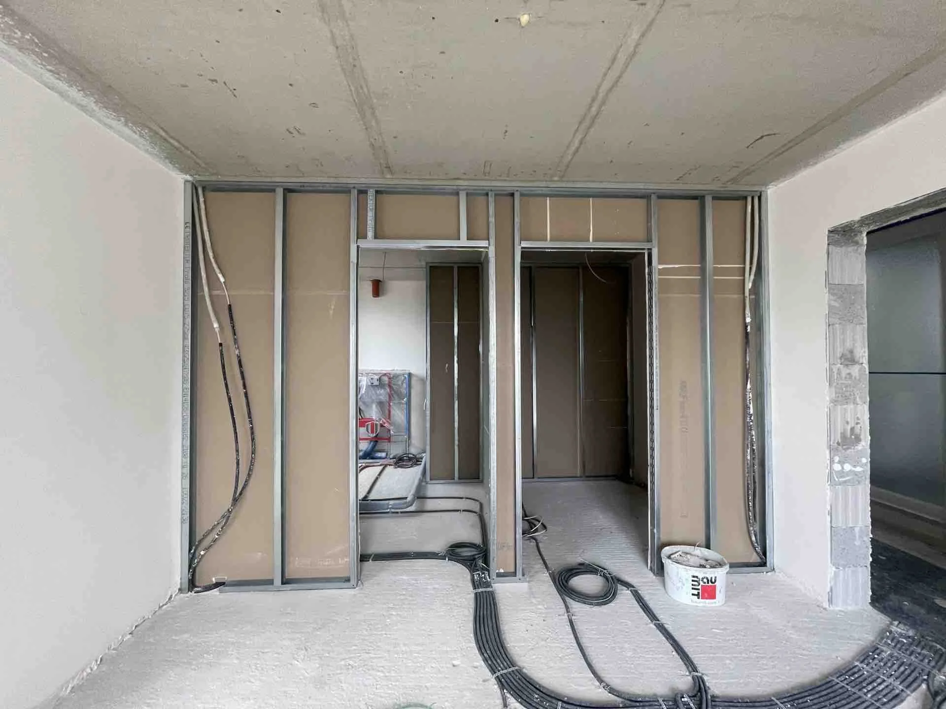 Innenraum eines Gebäudes unter Renovierung, mit Metallständerwänden, Kabeln und Baumaterialien auf dem Boden.