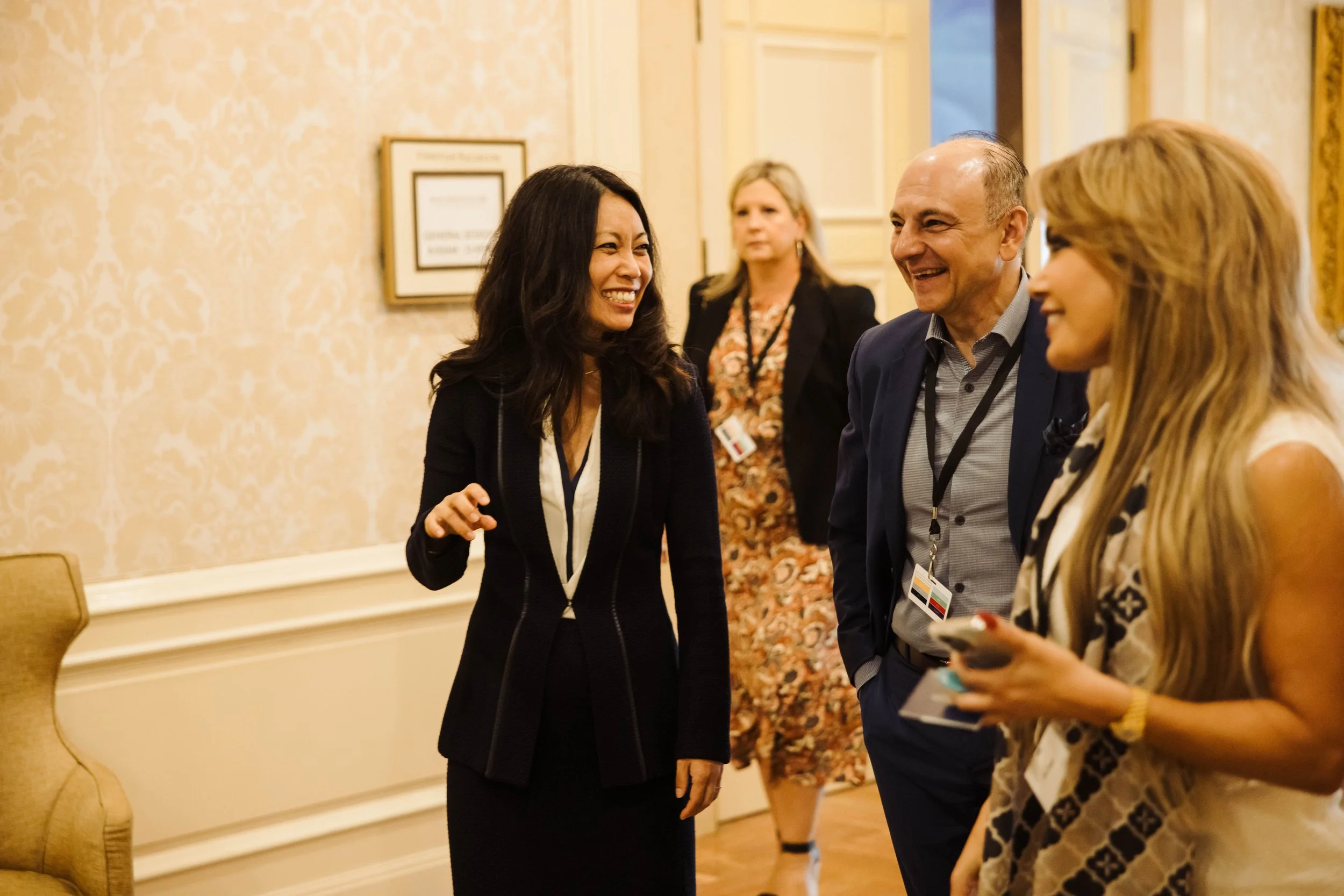 Four people engaged in conversation in a formal indoor setting, with two women and two men, smiling and wearing business attire. The Breakers Palm Beach, corporate event photography
