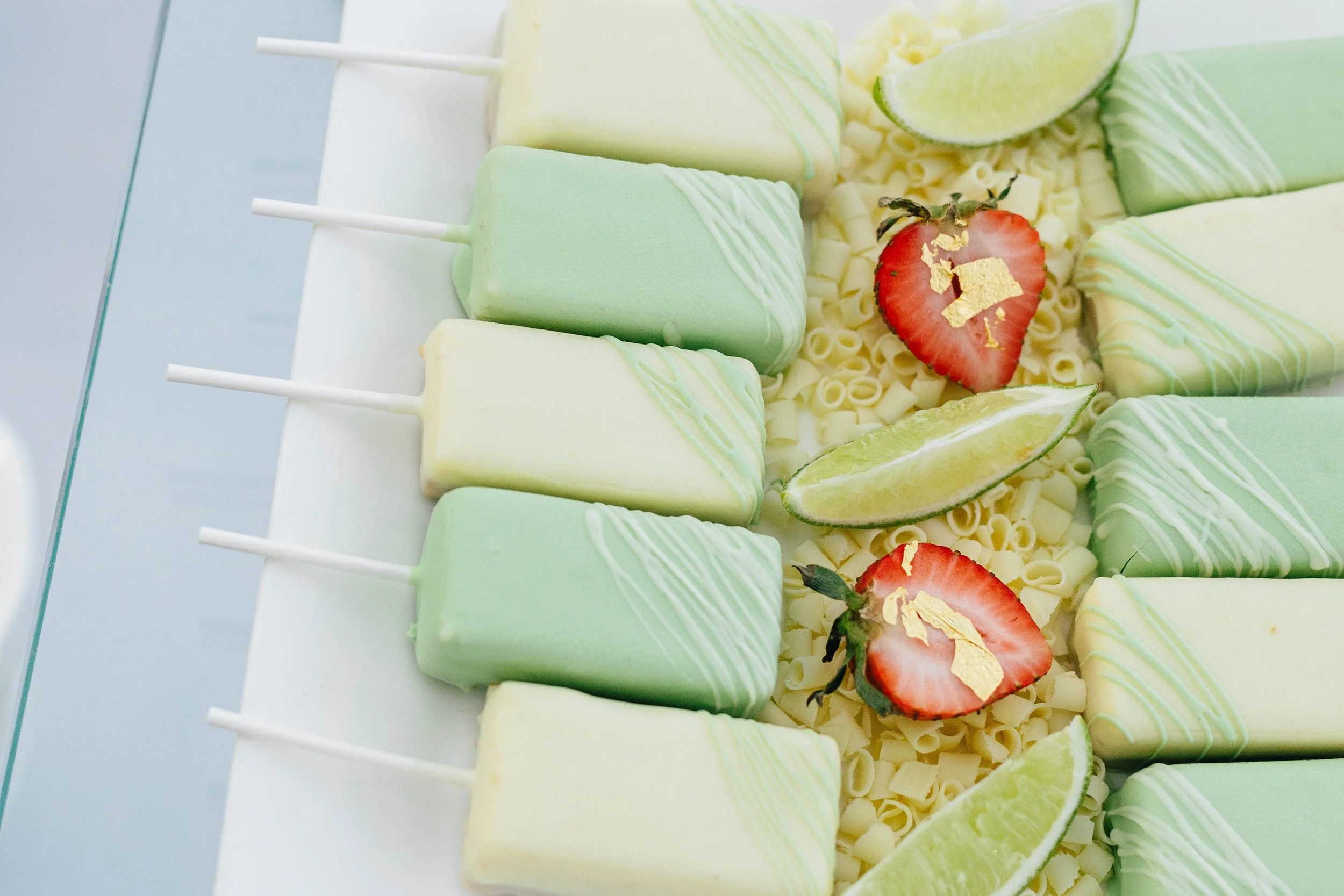 Close-up of green and white ice cream bars on sticks, garnished with strawberries, lime wedges, and white chocolate curls. The Breakers Palm Beach, corporate event photography