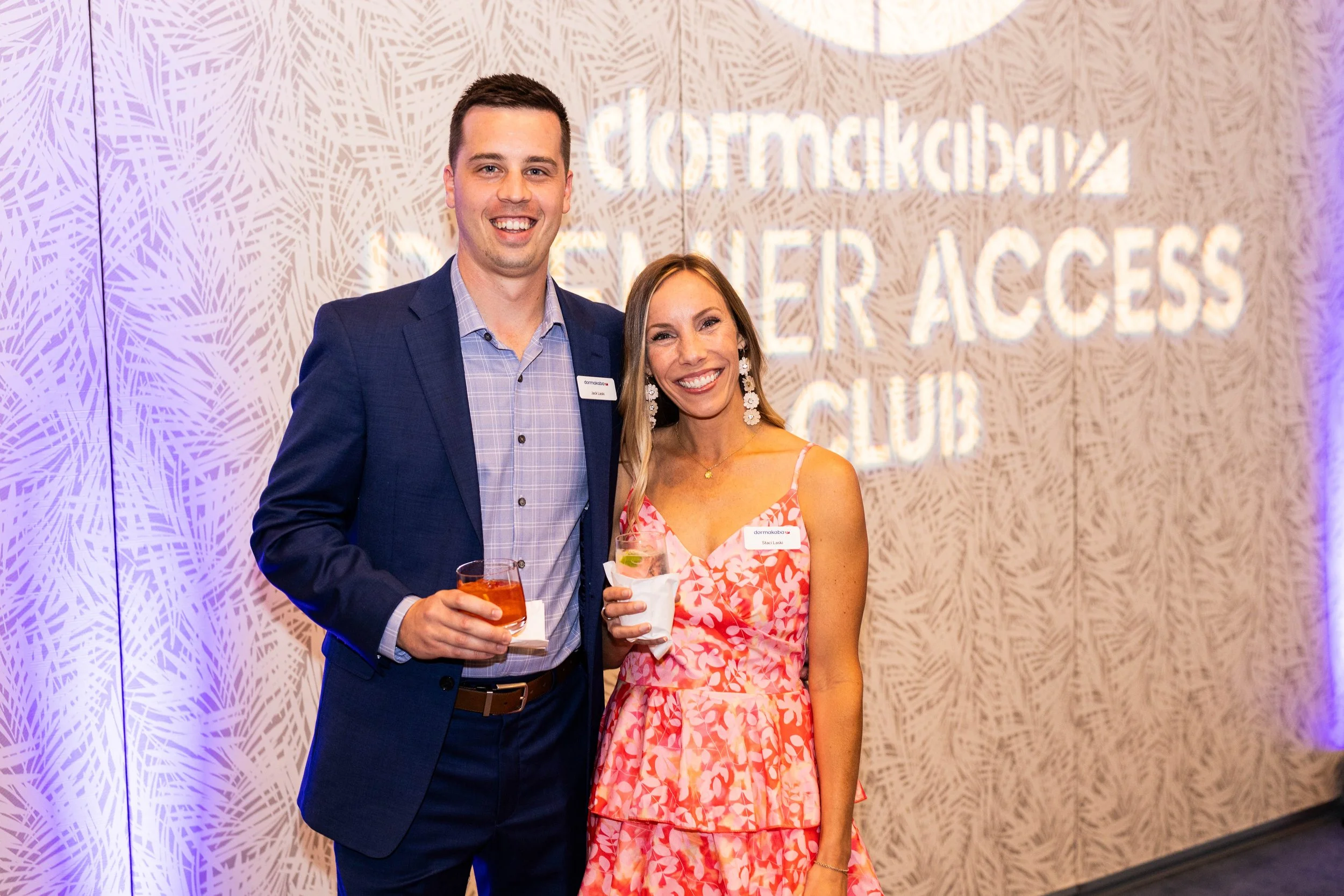 Two people smiling and holding drinks at a professional event, standing in front of a wall with a sign that reads 'dormakaba' and 'LEADER ACCESS CLUB.' at The Breakers Palm Beach.
