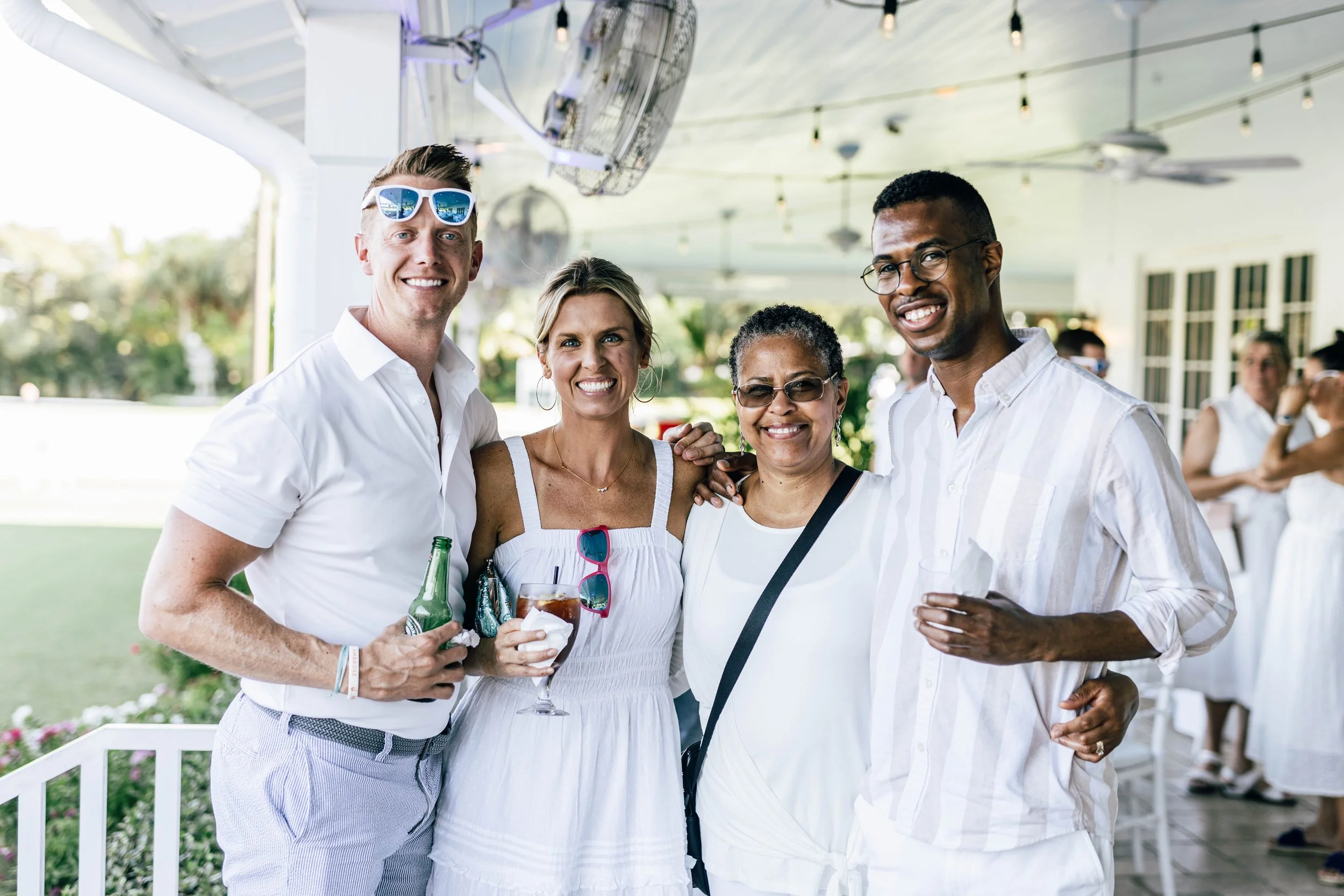 Group of four diverse people smiling and enjoying a social gathering outdoors under a covered patio at The National Croquet Club.