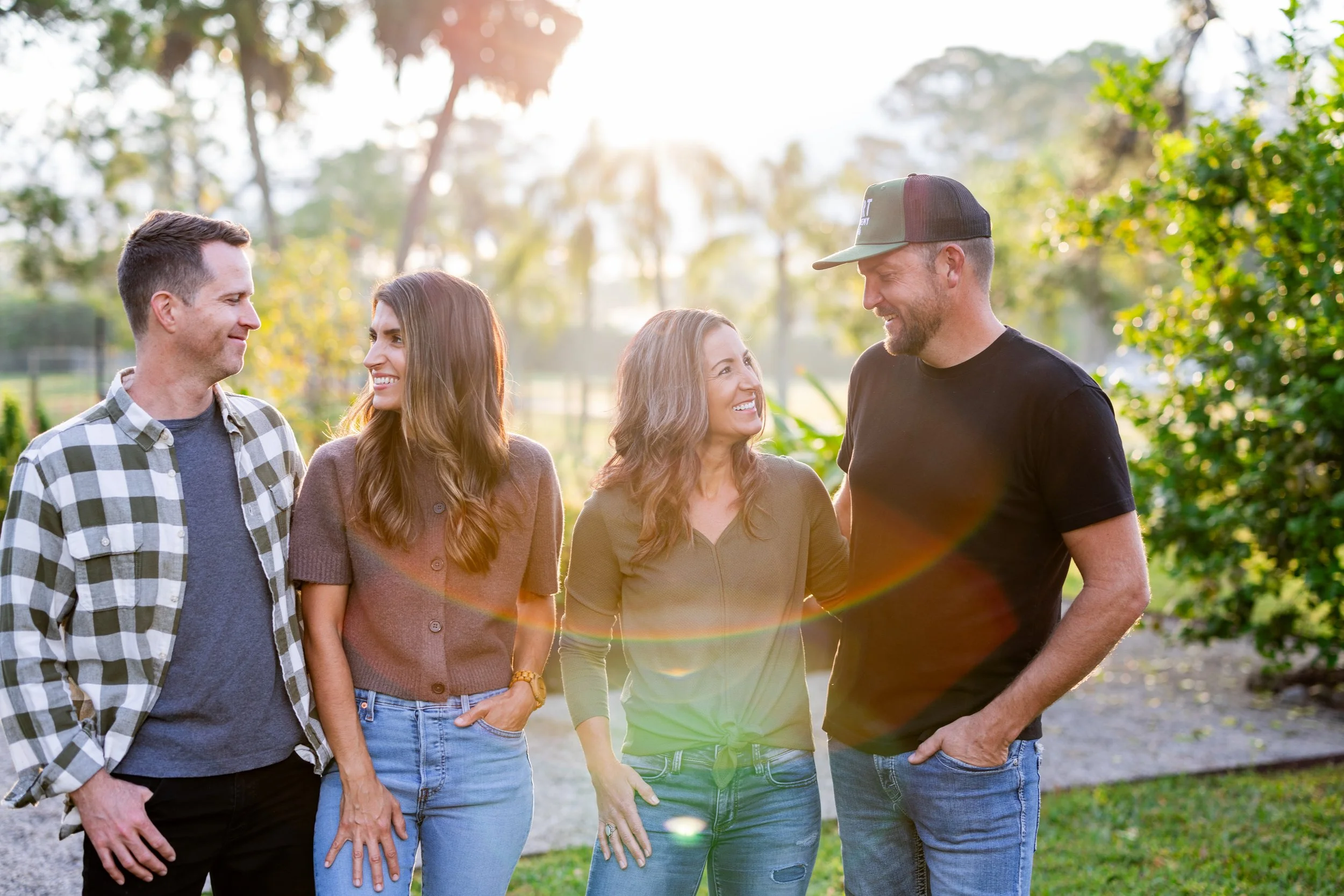 Group of four people smiling and talking outdoors in a park during sunset. Brand activation photography.