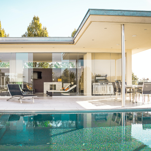Modern house with glass walls, outdoor swimming pool, and patio furniture