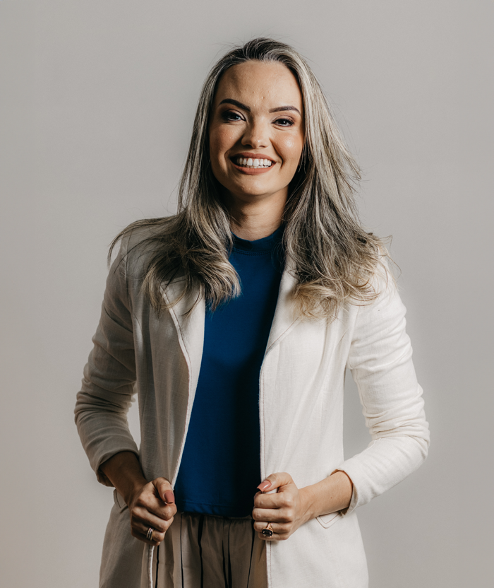 A woman with long blonde hair smiling at the camera, wearing a beige blazer over a blue shirt, against a neutral background.