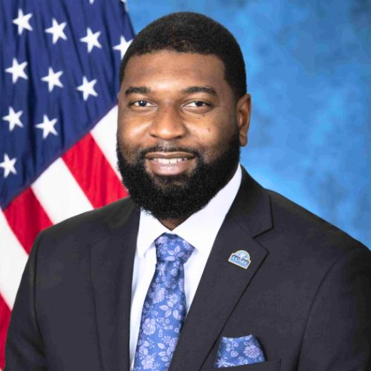 Portrait of a man in a suit with an American flag in the background.