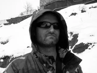 Man wearing sunglasses and a hooded jacket outdoors in a snowy landscape.