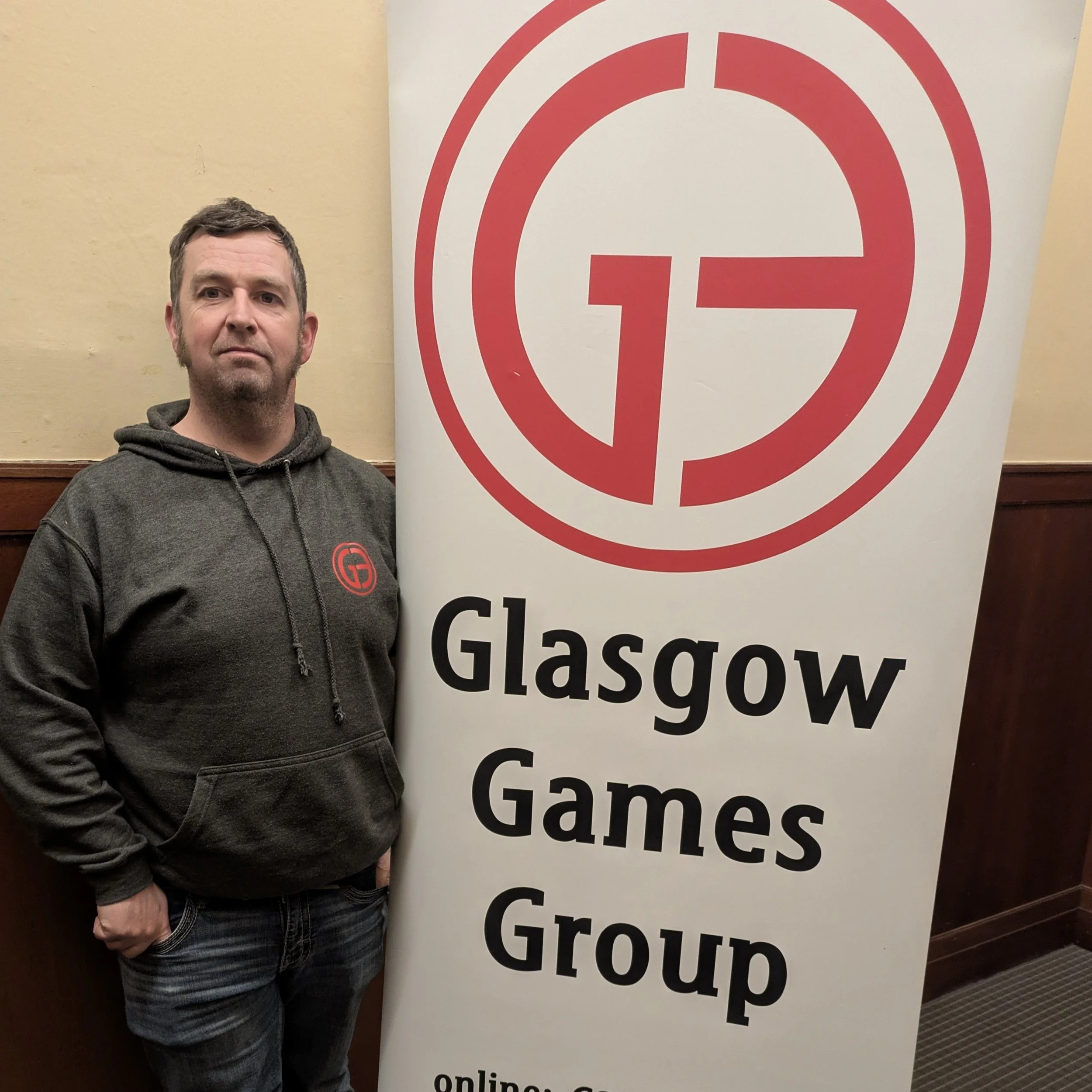 A man standing next to a vertical banner that reads 'Glasgow Games Group' with a red 'G' logo.