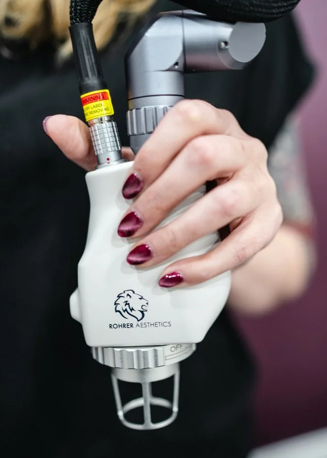 Person holding a device used for cosmetic or aesthetic procedures, branded with the logo and name 'Rohder Aesthetics'.