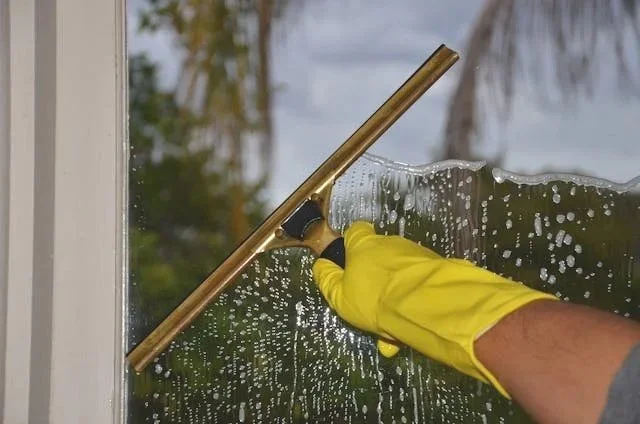 Person wearing yellow gloves cleaning a window with a squeegee.