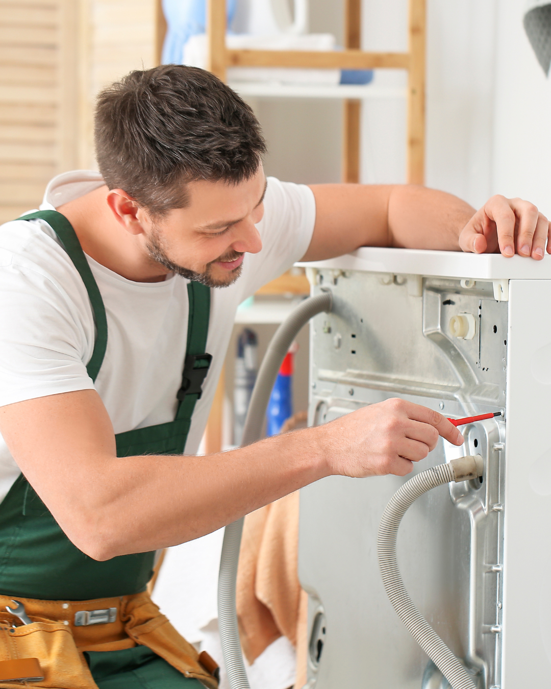A man repairing a washing machine, using a screwdriver inside the appliance.
