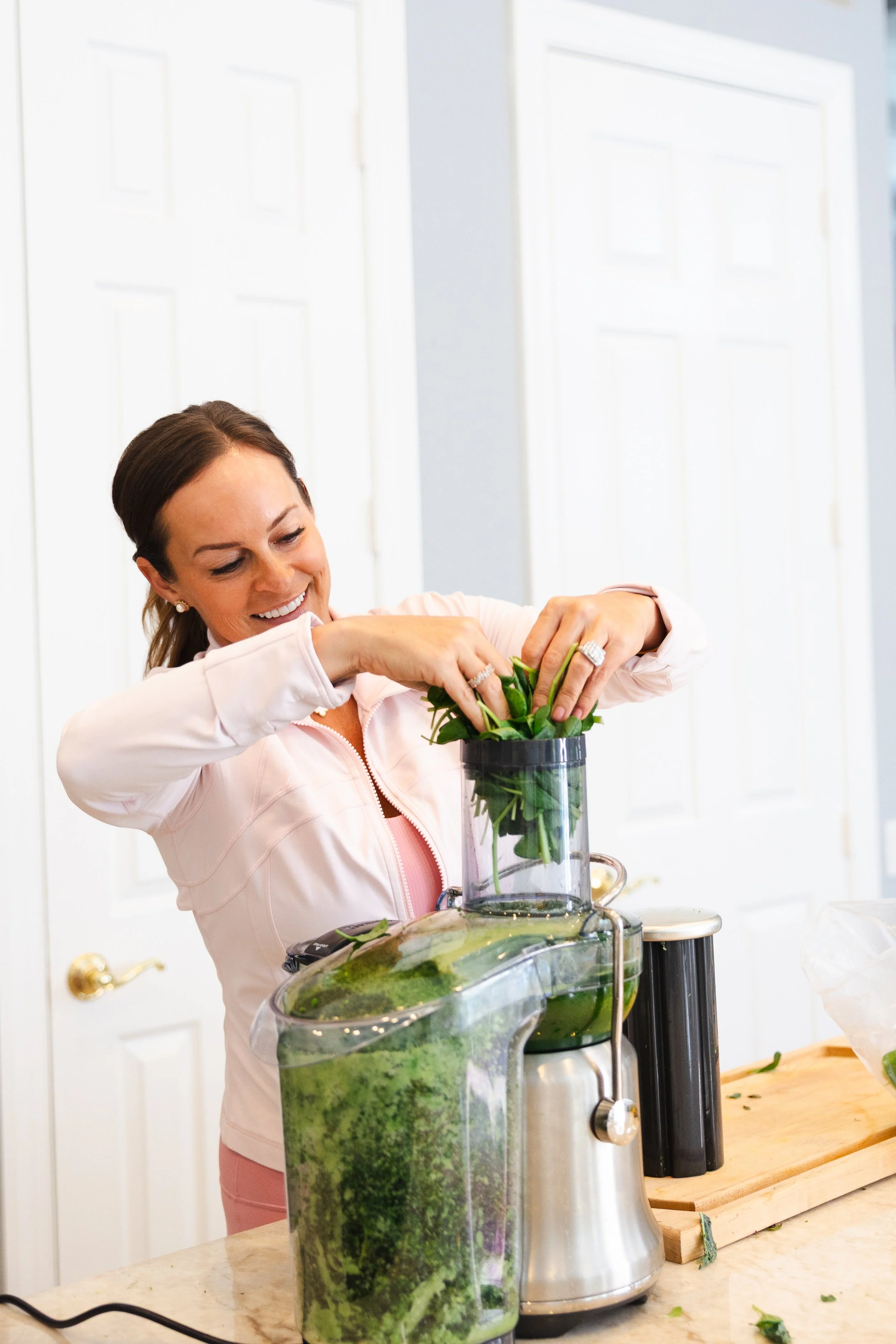 A woman using a juicer to prepare fresh green juice with leafy greens in a kitchen.