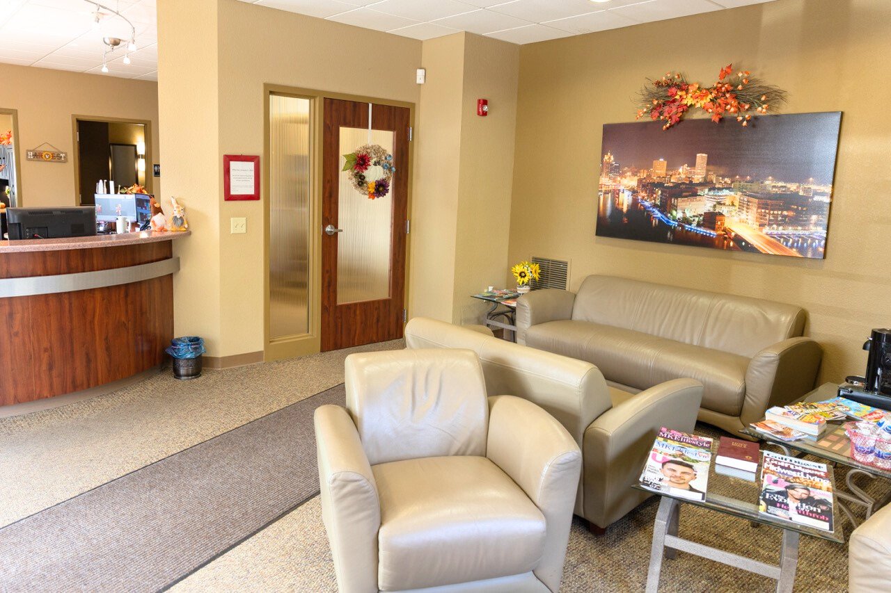 A cozy waiting area with beige walls, cream leather armchairs and a sofa, and a small glass table with magazines.
