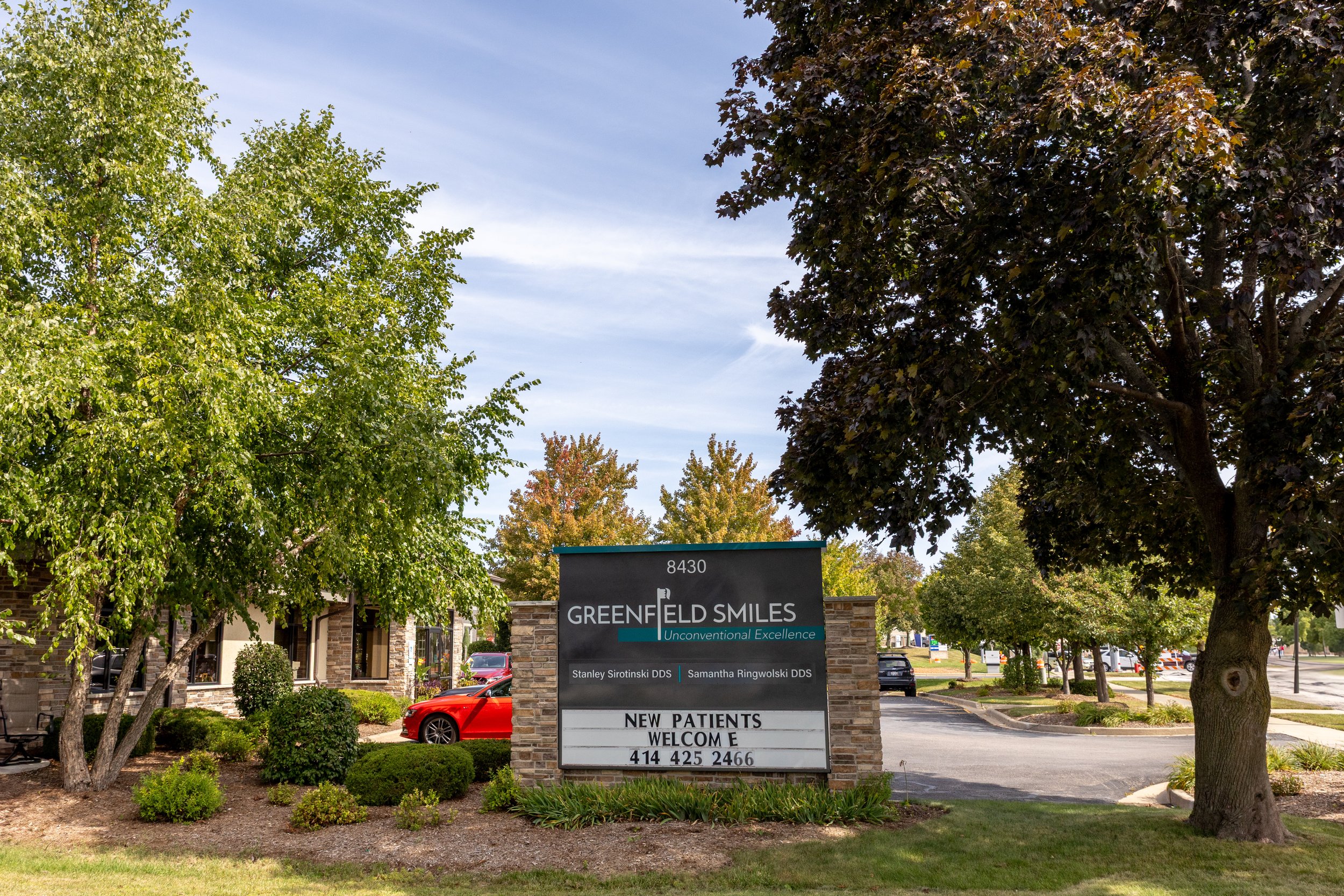 Signboard for Greenfield Smiles dental practice with trees and parking lot in the background.