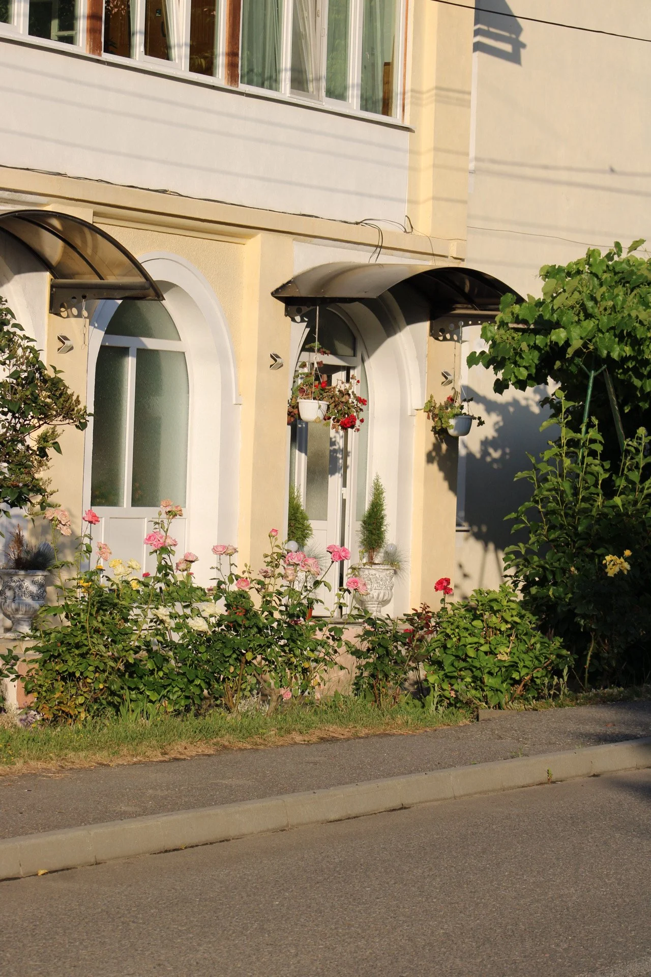 A house with decorated windows and a garden full of pink and white flowers in front of a sidewalk and street.