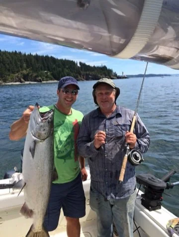 Two men standing on a boat holding a large fish, with water and trees in the background.