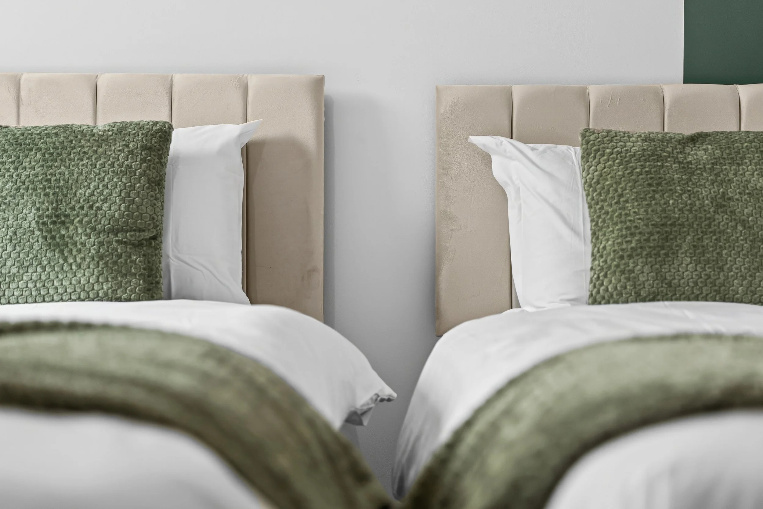 A bedroom with two beds, a window with white curtains, and a round mirror reflecting the room.