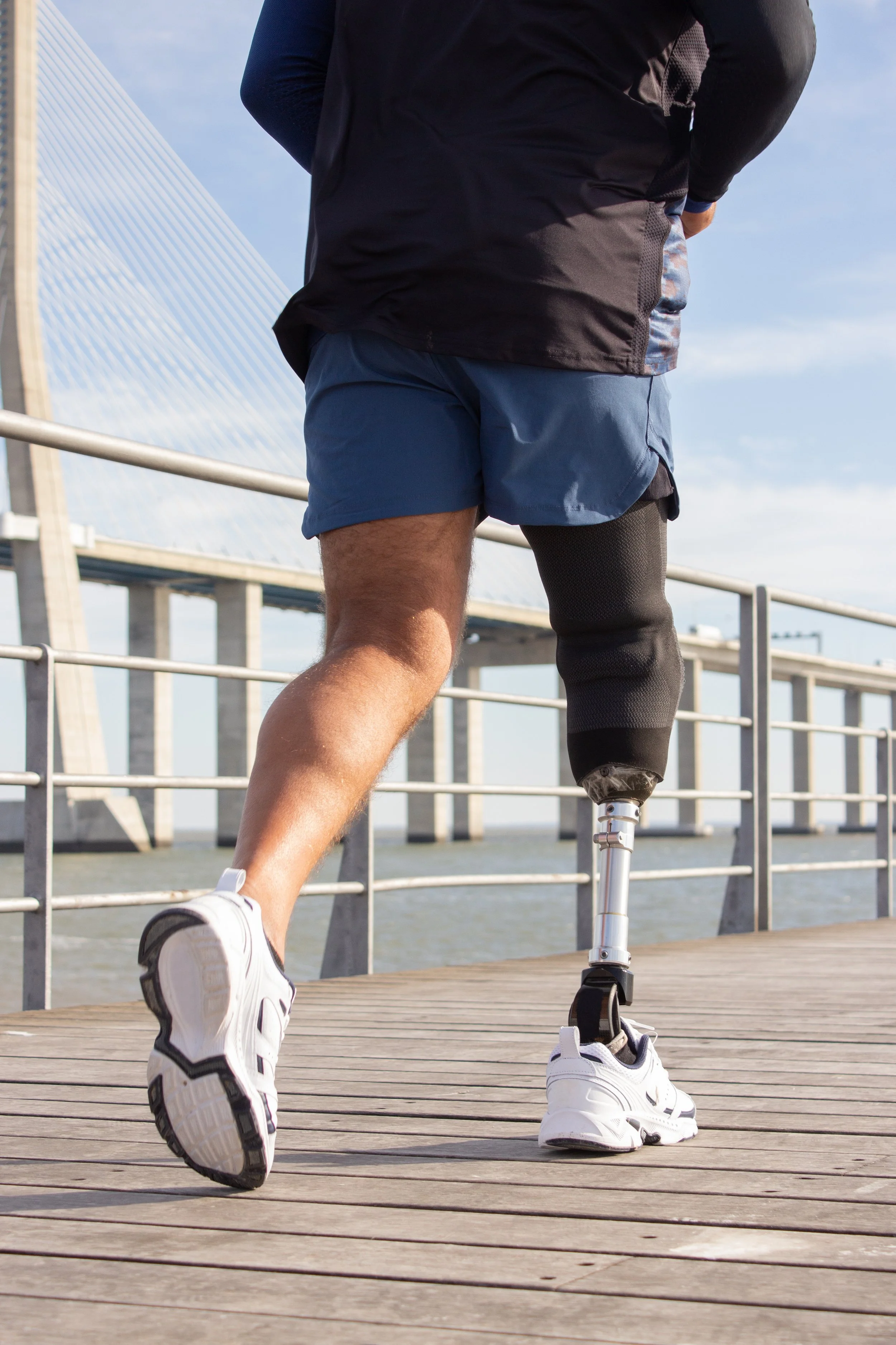 A person with a prosthetic leg running on a wooden bridge with a bridge structure in the background.