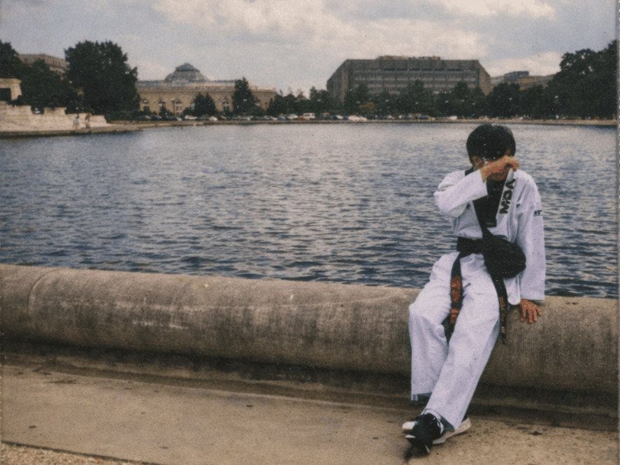 Aiden Kim sits at a harbor's edge wearing his Taekwondo uniform.
