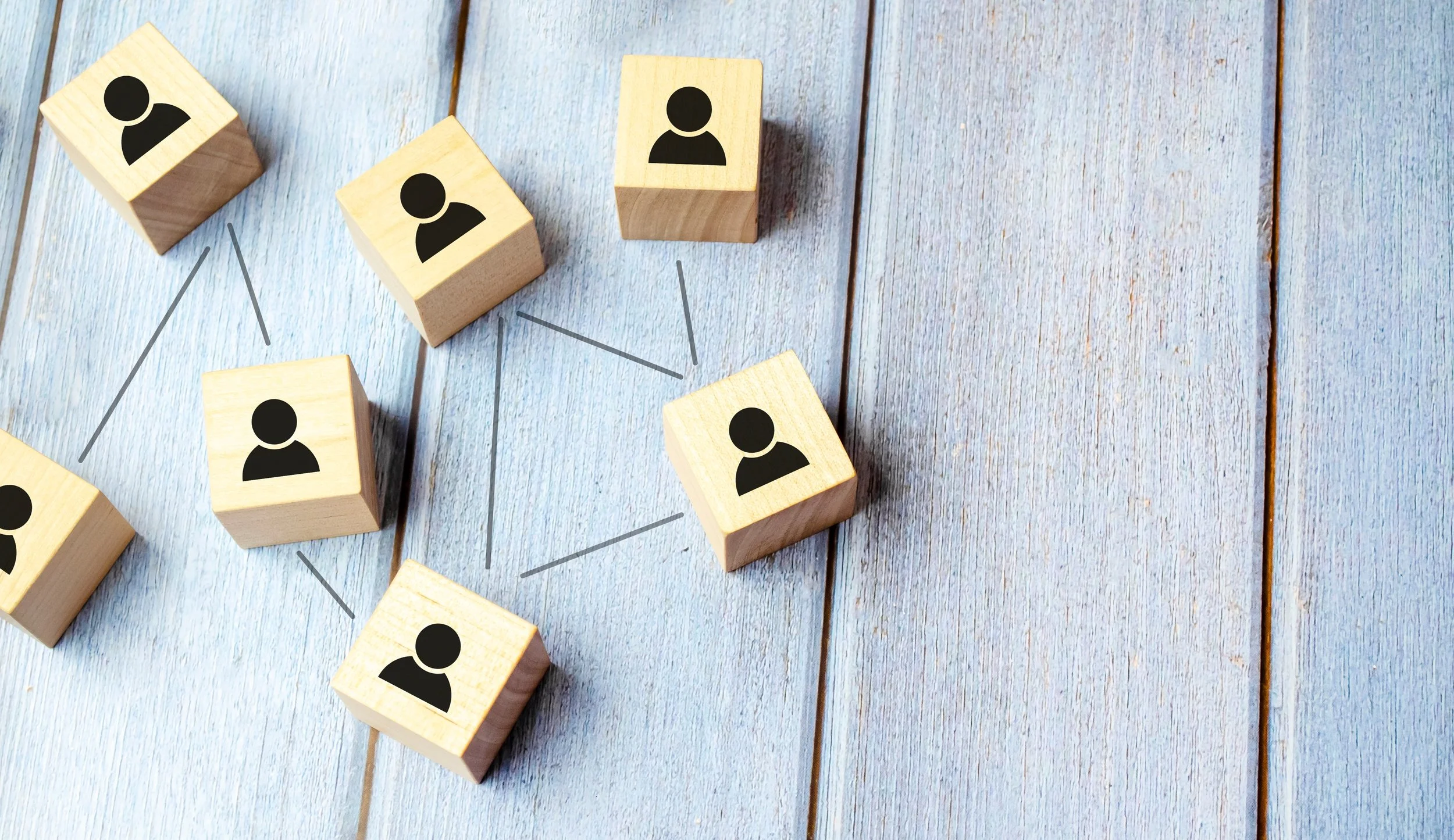 Wooden blocks with user icons connected by lines, representing a social network or organizational chart on a wooden surface.
