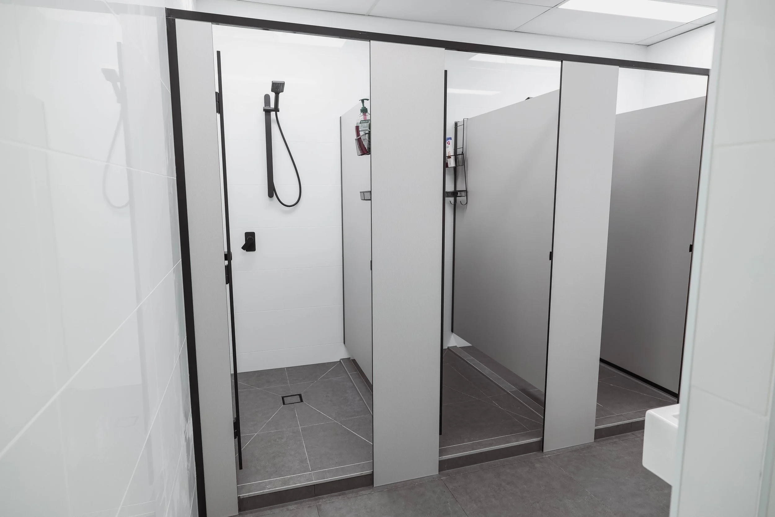 A men's bathroom with four partially open stall doors revealing a hand dryer, a fire extinguisher, and other bathroom fixtures.