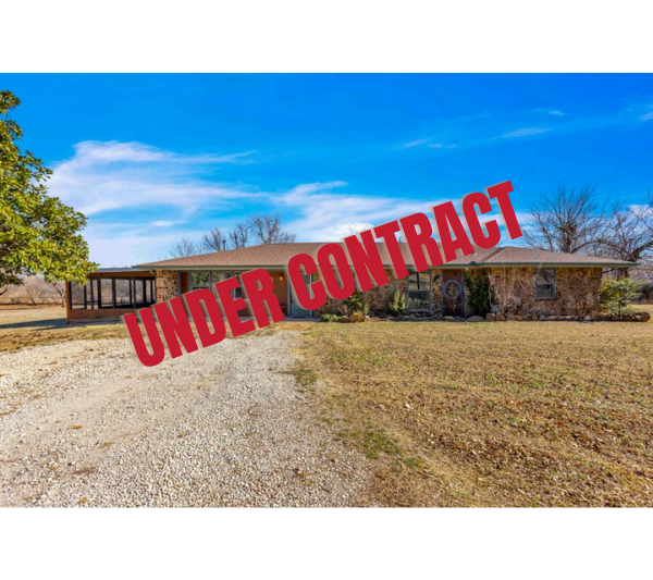 Single-story house with a stone and brick exterior, large front yard with gravel driveway, on a clear day with blue sky and leafless trees.