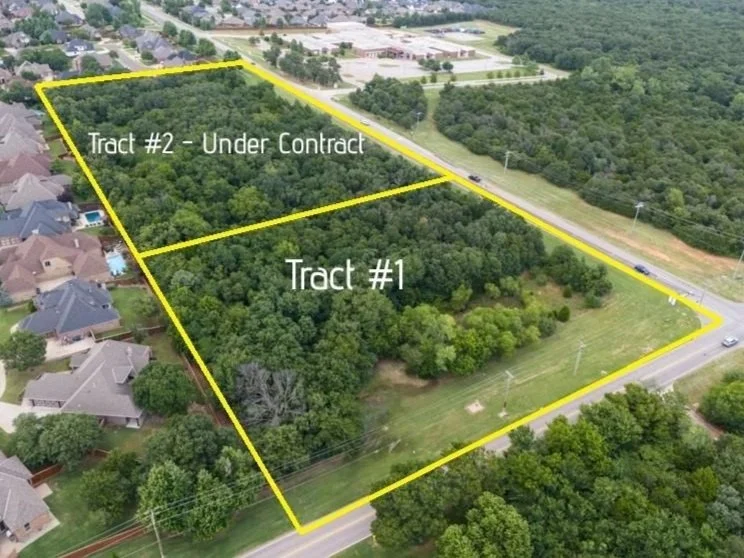 Aerial view of a large wooded area with a property boundary marked in yellow, adjacent to a residential neighborhood and a major road with traffic.
