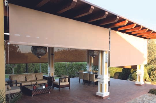 Outdoor patio with beige retractable awnings, wooden flooring, cushioned seating, and surrounding greenery