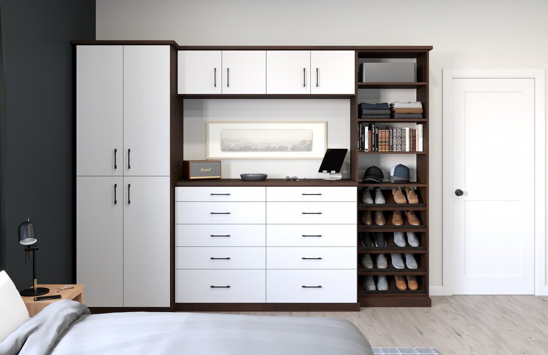 A modern closet with white cabinets, open shelves filled with shoes, stacks of folded clothes, and a framed picture on a dark brown wall unit in a bedroom.