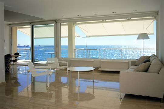Living room with large windows overlooking the ocean, white furniture, a coffee table, and a floor lamp.